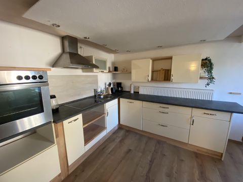 Eine moderne Küche mit Edelstahl-Geräten und hellen Schränken. Der Boden ist aus Holz und es gibt viel Platz auf der Arbeitsfläche.