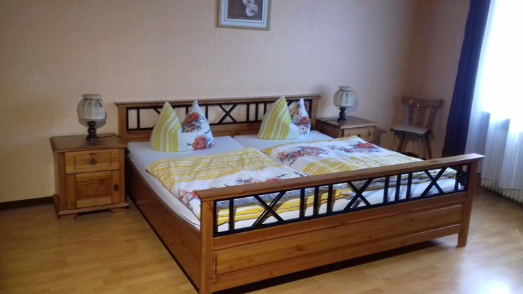 Ein gemütliches Schlafzimmer mit einem großen Doppelbett aus Holz. Angenehme Farben und viel Tageslicht sorgen für eine einladende Atmosphäre.