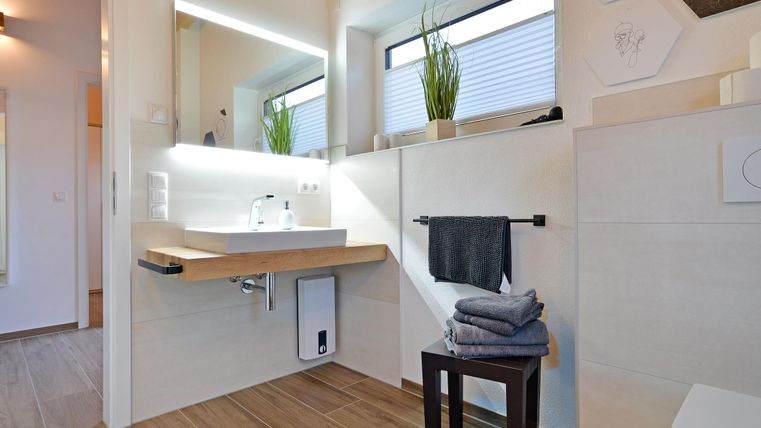 Ein modernes Badezimmer mit einem schlichten Waschtisch und großen Fenstern. Auf der Oberfläche liegen Handtücher und ein kleiner Hocker.