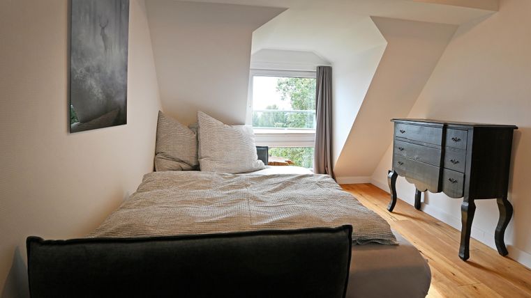 Ein gemütliches Schlafzimmer mit einem Doppelbett und einem kleinen Schrank. Das Fenster bietet einen Blick ins Freie und lässt viel Licht herein.