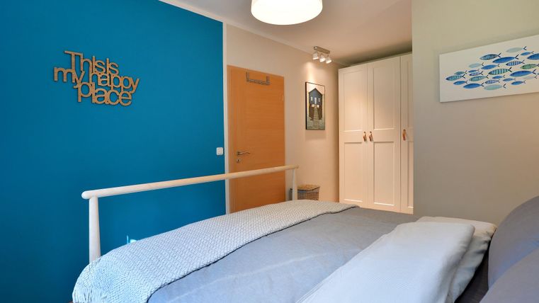 Ein gemütliches Schlafzimmer mit einem blauen Akzentwand und einem großen Bett. Es gibt einen dekorativen Schriftzug und einen Kleiderschrank im Hintergrund.