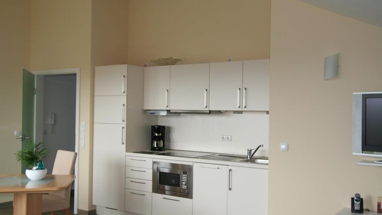 Eine moderne Küche mit weißen Schränken und einer klaren Arbeitsfläche. Ein Tisch und Stühle ergänzen den Raum.