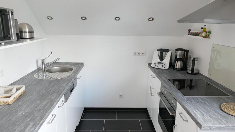 Een moderne keuken met grijze werkbladen en witte kasten. De keukenapparatuur is overzichtelijk gerangschikt, en de verlichting zorgt voor een uniforme lichtinval.