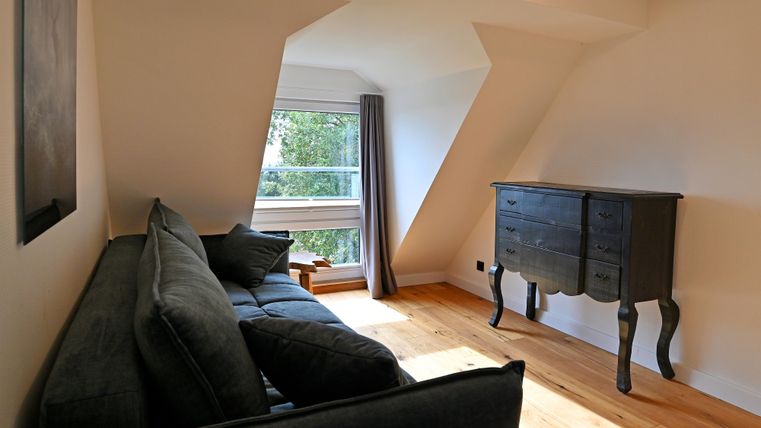 Ein gemütliches Wohnzimmer mit einem dunkelgrauen Sofa und einem eleganten Sideboard. Ein großes Fenster lässt viel Tageslicht herein.