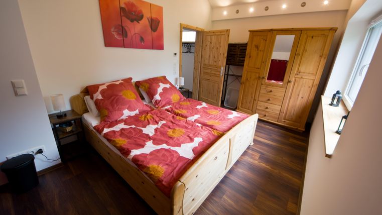 Ein gemütliches Schlafzimmer mit einem großen Bett und farbenfrohen Bettdecken. Die Wände sind hell gestrichen und es gibt Holzmöbel, die eine warme Atmosphäre schaffen.