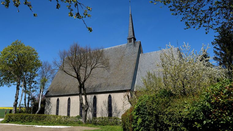 Eine alte Kirche umgeben von Bäumen und grüner Wiese. Der Himmel ist klar und blau.