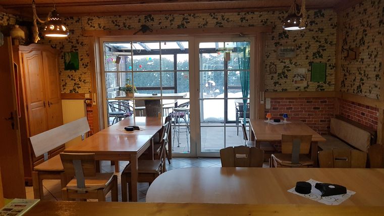 Ein gemütlicher Raum mit Holztafeln und Stühlen. Große Fenster geben einen Blick auf den Außenbereich.